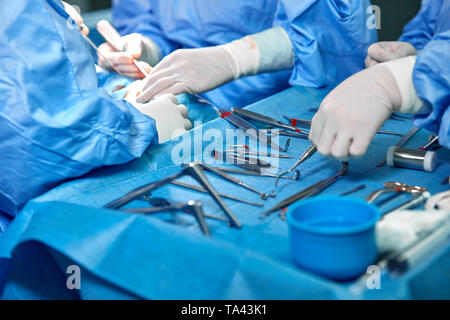 In der Nähe von Doktor Hände während der Operation in Betrieb. Sterilen chirurgischen Instrumenten in einem realen Betrieb verwendet. Schwerpunkt liegt auf der Zeile der Klemmung Griffe. Stockfoto