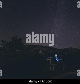 Abstrakter Mann, der auf einer Bank unter einem schönen Himmel sitzt Voller Sterne Stockfoto