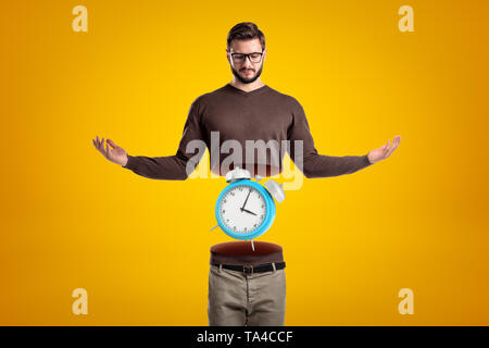 Junger Mann in Freizeitkleidung in der Hälfte mit blauen Wecker innen auf gelben Hintergrund ausschneiden Stockfoto