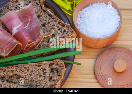 Snack mit selbstgemachten Roggenbrot und getrocknet Schweinefleisch auf einem braunen Ton Platte close-up Stockfoto