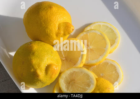 Ganze und aufgeschnittene Zitronen auf weißem Platter Stockfoto