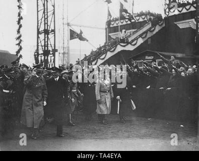 Adolf Hitler (mit seiner linken Hand angehoben) kommt an der Seite von howaldtswerke Hamburg für den Start des Schiffes. Begleitet wird er von der Reichsorganizationsleiter und der Namensgeber des Schiffes, Robert Ley, sowie SS-Obergruppenfuehrer Josef epp' Dietrich (beide rechts im Bild). Im Hintergrund, eine verzierte Tribüne, vor einer Menschenmenge begrüßt die Führer. Stockfoto