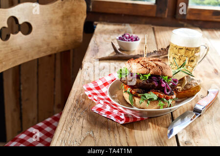 Spezialität wild Beef Burger auf ein knuspriges Brötchen mit schaumigem Bier und Kartoffel Kanten für eine rustikale Taverne Mittagessen Stockfoto