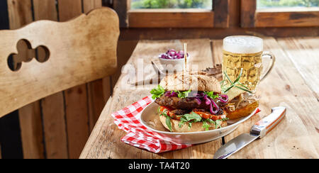 Wild Burger mit wild Patty und Salat Zutaten auf ein knuspriges Brötchen serviert mit einem Becher schaumiges Bier an einem rustikalen Tisch Stockfoto