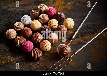 Handgemachte Schokolade praline Praline Display mit einer ordentlichen Rechteck der sortierten Fondant auf rustikalem Holz mit Draht Heber und Gabel Stockfoto