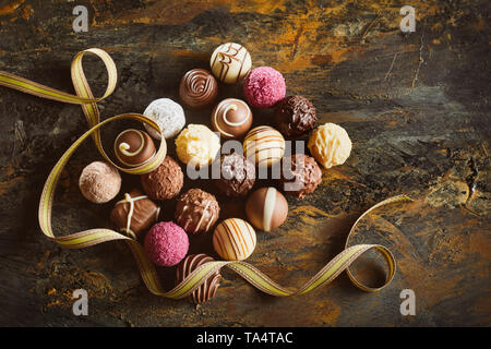 Elegante Darstellung von Luxus Pralinen in einem ordentlichen Rechteck mit wirbelnden Gold Ribbon auf rustikalem Holz von oben gesehen angeordnet Stockfoto