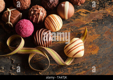 Gourmet handgemachte Schokolade Pralinen in Herzform auf einem Twirled Gold Ribbon mit einer Auswahl an Schokoladenspezialitäten über rustikale Holz für Valentines Tag Stockfoto