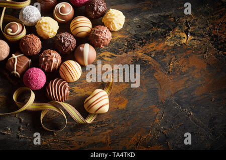 Gourmet Schokolade Valentinstag noch Leben mit einer großen Auswahl an Luxus handgefertigte Pralinen mit einem Herzförmigen Bonbon auf einem Twirled ribbon Sym Stockfoto