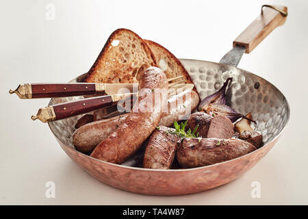 Kupfer Pfanne mit sortierten deutschen Würste mit Roggen Brot Toast und Utensilien über weiß serviert. Stockfoto