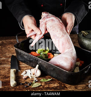 Koch Anzeige einer frischen rohen wilden Kaninchen Karkasse, wie er bereitet sie für den Braten in einer Pfanne mit Lauch, Karotten, Knoblauch, Kräutern und Gewürzen Stockfoto