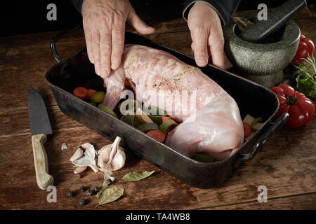 Der Küchenchef bereitet ein wildes Kaninchen für die Röstung reiben Gewürze auf das Fleisch in einen Bräter mit Lauch, Karotten, Tomaten Kräuter und Knoblauch Stockfoto