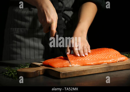 Frau schneid Filet vom frischen Lachs am Tisch Stockfoto