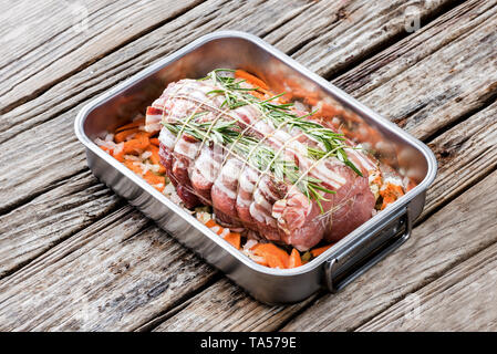 Schweinerücken Braten mit Net, Gemüse garnieren in Kasserolle auf hölzernen Hintergrund Stockfoto
