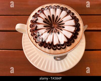 Latte, Cappuccino mit kunstvoll verzierten Milchschaum in die Schale auf Holztisch, Bangkok Stockfoto