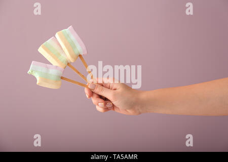 Weibliche Hand, die eine leckere Marshmallow Lutscher auf farbigen Hintergrund Stockfoto