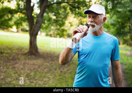 Gut aussehender älterer Mann Ausruhen nach dem Joggen im Park an einem sonnigen Tag. Stockfoto