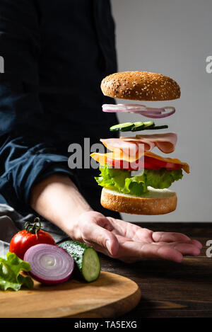 Frei schwebende Burger in der Hand des Mannes. 'S Flying burger Zutaten Stockfoto