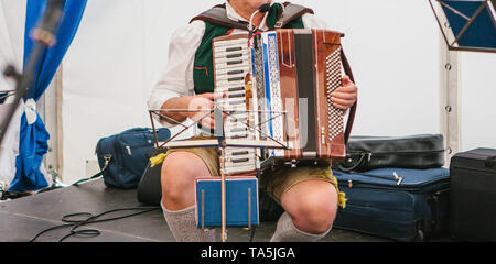 Akkordeonspieler in Traditionelle bayerische Kleidung spielt das Akkordeon auf der Bühne. Der Akkordeonist spielt das Musikinstrument. Stockfoto