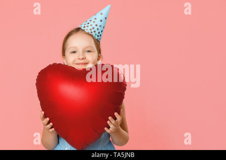 Happy kleines Mädchen in einem Gap hält ein großes Herz geformten Ballon. Porträt eines Kindes auf einem rosa Hintergrund. Kopieren Sie Platz. Nahaufnahme. Stockfoto