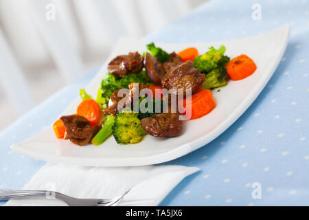 Gebratenes Huhn Herzen mit gekochten Brokkoli und gebackene Karotten auf weiße Platte serviert. Stockfoto