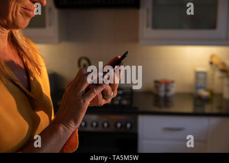 Reife Frau mit Handy in der Küche zu Hause. Stockfoto