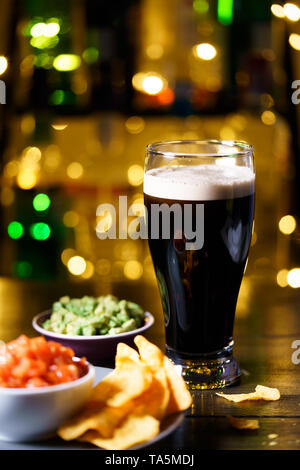 Glas stout mit Nachos, Tomaten Salsa und Guacamole. Bar Flaschen in Bokeh, hohe Auflösung Stockfoto
