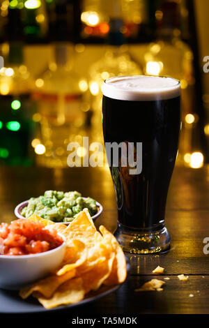 Glas stout mit Nachos, Tomaten Salsa und Guacamole. Bar Flaschen in Bokeh, hohe Auflösung Stockfoto