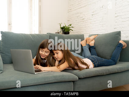 Süße kleine Mädchen und ältere Schwester spielen zusammen lächeln und in Verbindung mit einem Laptop auf der Couch zu Hause. Glückliche Familie Geschwister Beziehung Stockfoto