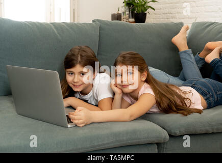 Süße kleine Mädchen und ältere Schwester spielen zusammen lächeln und in Verbindung mit einem Laptop auf der Couch zu Hause. Glückliche Familie Geschwister Beziehung Stockfoto