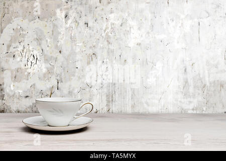 Vintage Teetasse auf einem weißen Holztisch, texturierte Wand Stockfoto