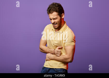 Junge wütend schöner Mann leidet unter Schmerzen im Bauch, isolierte blauen Hintergrund, Nahaufnahme, Seite, Ansicht Foto. Stockfoto