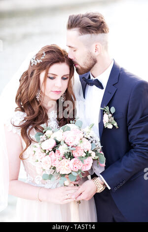 Schöne Braut holding Wedding Bouquet mit Bräutigam im Freien posieren. Hochzeitstag. Feier. 20. Stockfoto