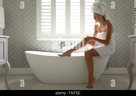 Schöne Frau ihre Beine massieren auf der Badewanne im Bad Stockfoto