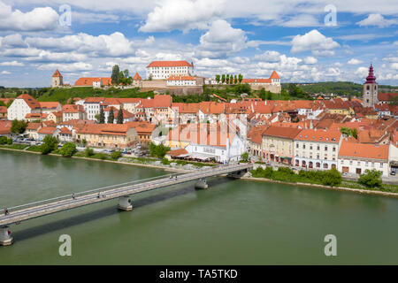 Luftaufnahme von oben auf die Altstadt von Ptuj. Panoramablick auf das Schloss von Ptuj auf Hügel, Drau, Fußgänger- und Radwege Brücke. Stockfoto