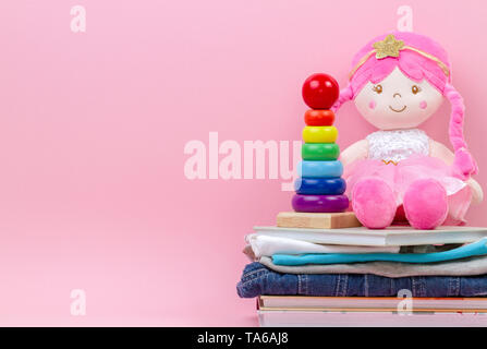 Spende, liebe Konzept. Weiche Puppe, Baby stapeln Ringe Pyramide, Kind Kleidung und Bücher über rosa Hintergrund gefüllt Stockfoto