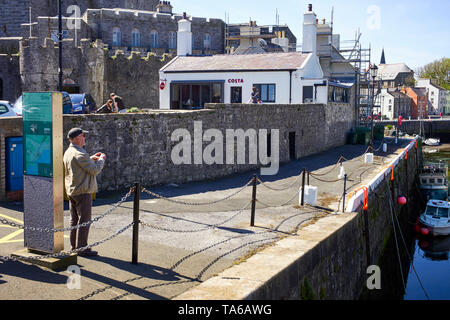 Ein älterer Mann, ein Foto von Castletown Hafen mit Costa Coffee und die Burg im Hintergrund Stockfoto