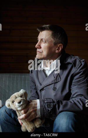 Reifen Mann sitzt auf einem Sofa, holding Spielzeug Tier- und weg schauen. Stockfoto