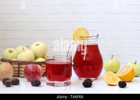 Kompott aus Beeren und Äpfel in eine Kanne und in einem Glas auf einem Tisch auf einem weißen Hintergrund, Foto gibt es Äpfel, Brombeeren und Zitrone Stockfoto