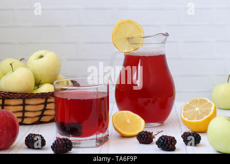 Kompott aus Beeren und Äpfel in eine Kanne und in einem Glas auf einem Tisch auf einem weißen Hintergrund, Foto gibt es Äpfel, Brombeeren und Zitrone Stockfoto
