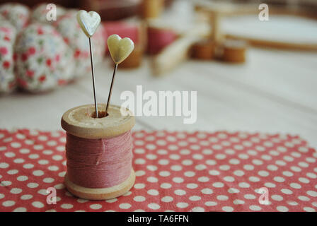 Nähen TOOLS Hintergründe. Nadeln, Spulen, PINK POLKA DOT STOFF, HERZ PINS GEGEN HOLZSCHREIBTISCH. Stockfoto