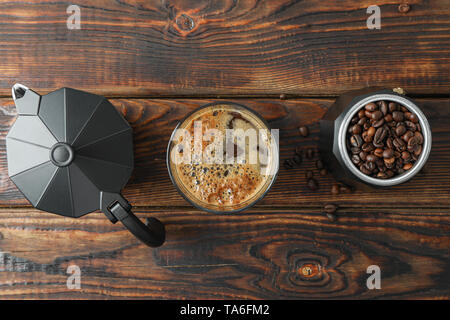 Flach Zusammensetzung mit einem Glas frischen Kaffee, Kaffeemaschine und Kaffee Bohnen auf Holztisch, Platz für Text Stockfoto
