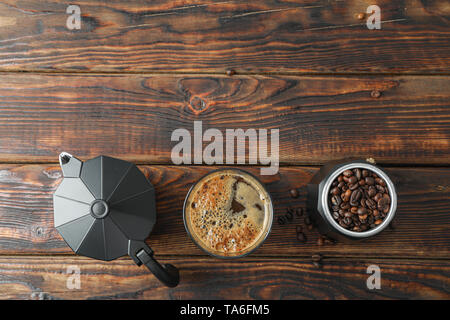 Flach Zusammensetzung mit einem Glas frischen Kaffee, Kaffeemaschine und Kaffee Bohnen auf Holztisch, Platz für Text Stockfoto