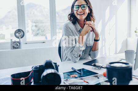 Weibliche Photo Editor an Ihrem Schreibtisch sitzen. Fotografin auf Kamera und lächelnd in Ihrem Büro. Stockfoto
