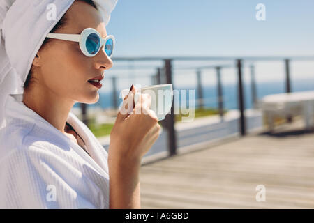 Schöne Frau sitzt am Pool/in. Weibliche Modell tragen Bademantel und Sonnenbrille entspannen am Pool. Stockfoto