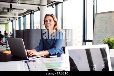 Junge Geschäftsfrau mit Laptop sitzen in einem Büro, in die Kamera zu schauen. Stockfoto
