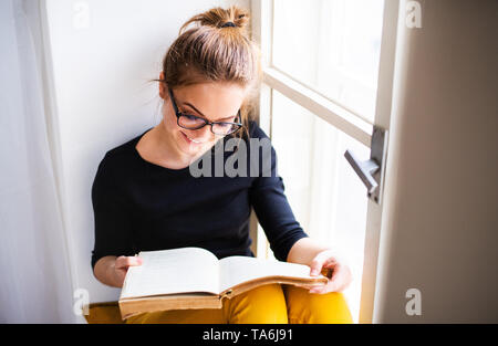 Eine junge Studentin mit Buch sitzen auf Fensterbank, studieren.
