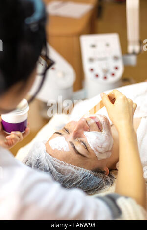 Kosmetiker die Maske auf das Gesicht des Kunden. Frau erhalten Gesichtspflege von kosmetikerin in Spa Salon Stockfoto