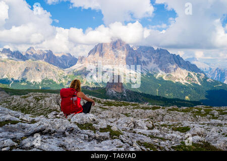 Weibliche Touristen mit roten Rucksack Anhalten auf dem Felsplateau unter Rifugio Nuvolau, Dolomiten, und Suchen in Richtung Cinque Torri, mit Castelletto, Tof Stockfoto