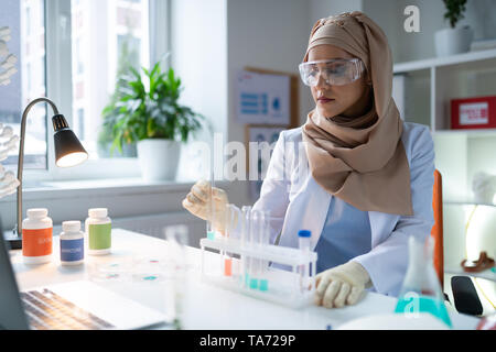 Beschäftigte Chemiker Handschuhe und Brille sitzen und arbeiten Stockfoto