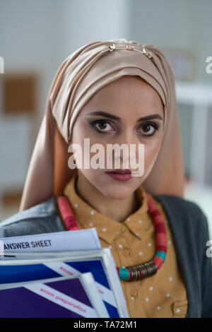 Dark-eyed muslimische Lehrerin holding Bücher stehen in der Schule Stockfoto